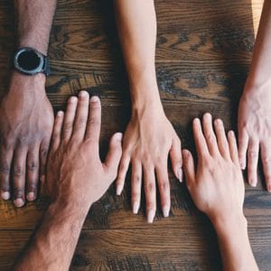 Four hands laying flat on a wooden table | New Member Groups